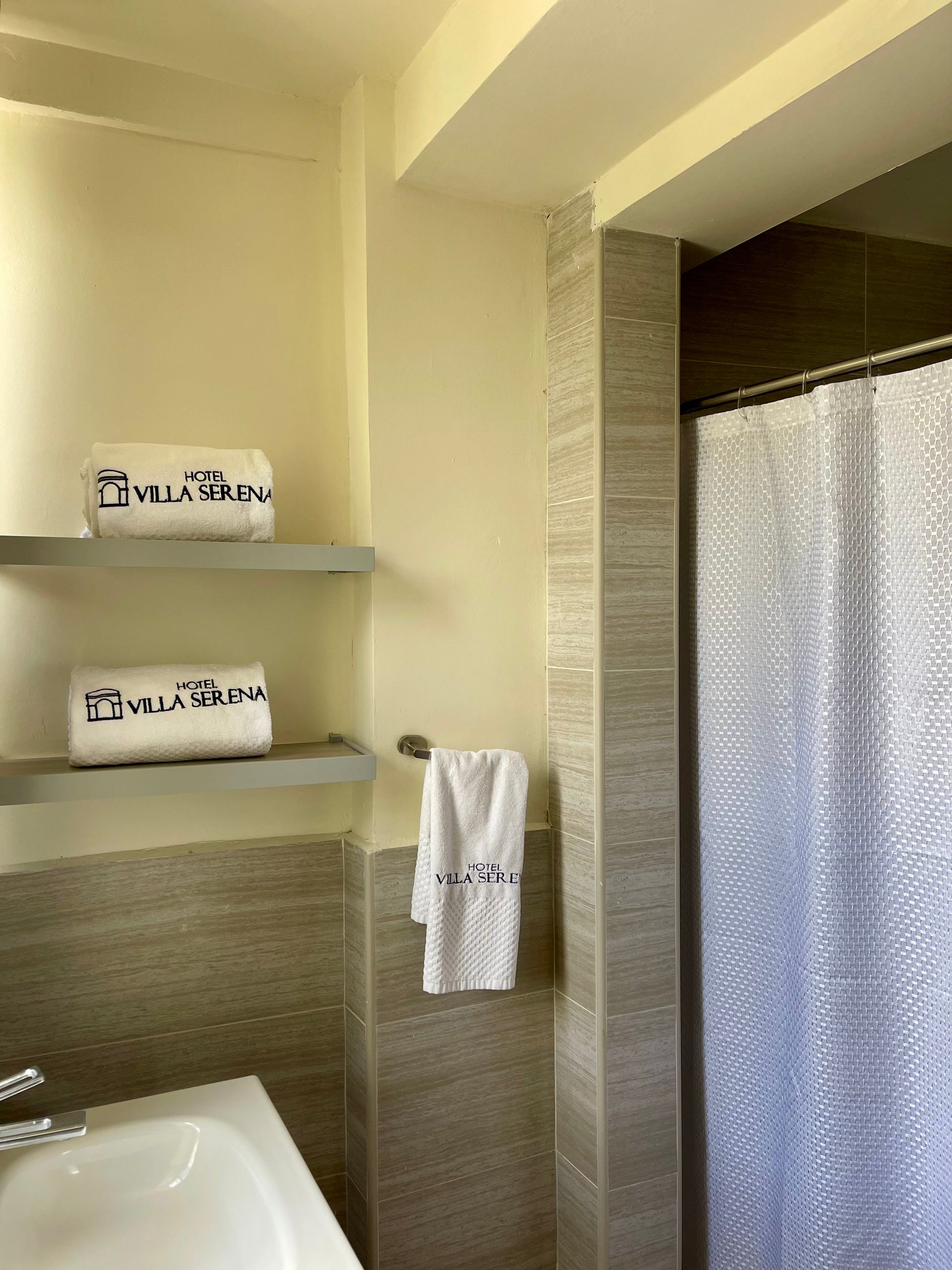 A bathroom with a bathtub , shower curtain , shelves and towels.