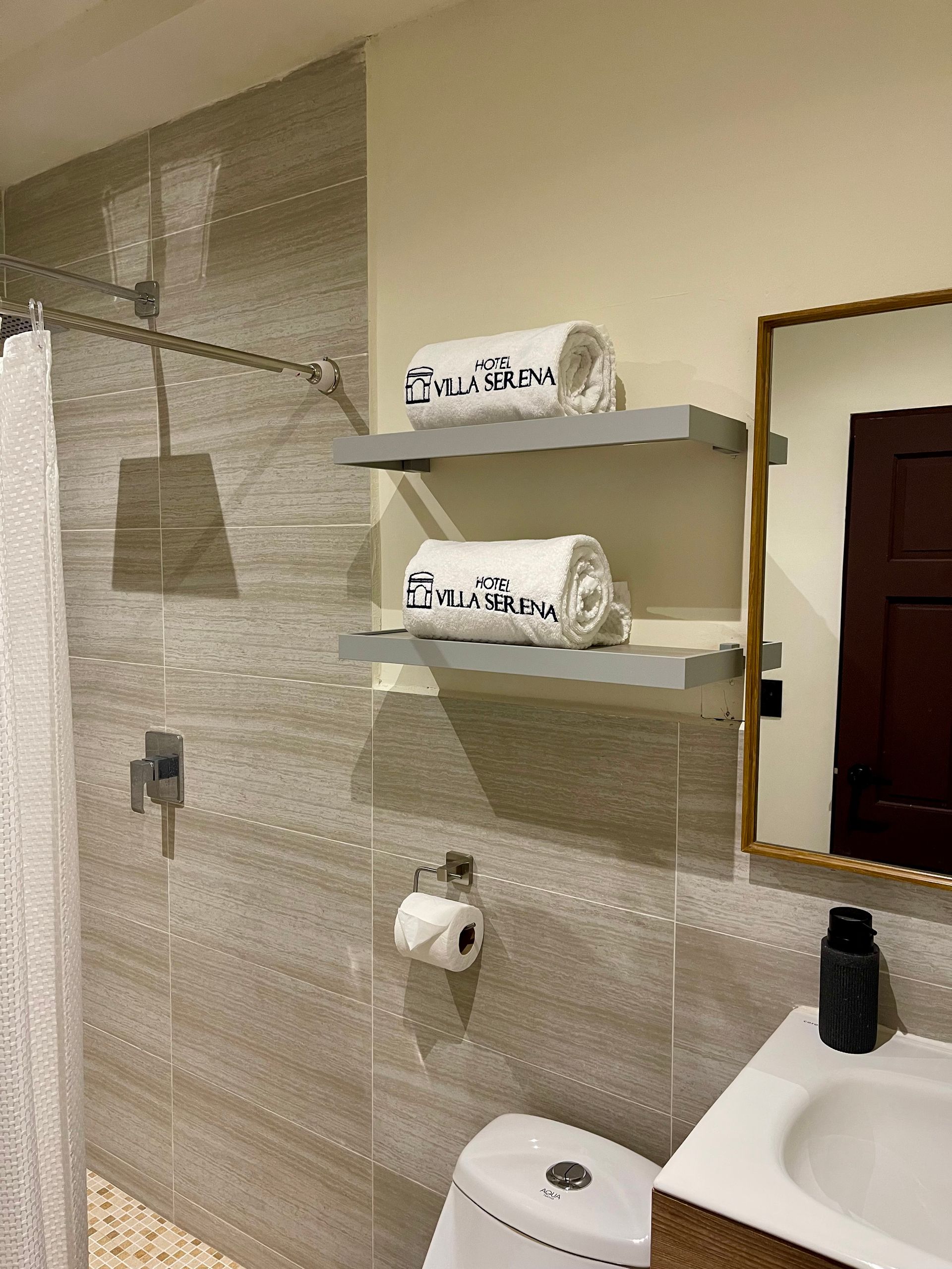 A bathroom with a toilet , sink , mirror and shelves with towels on them.