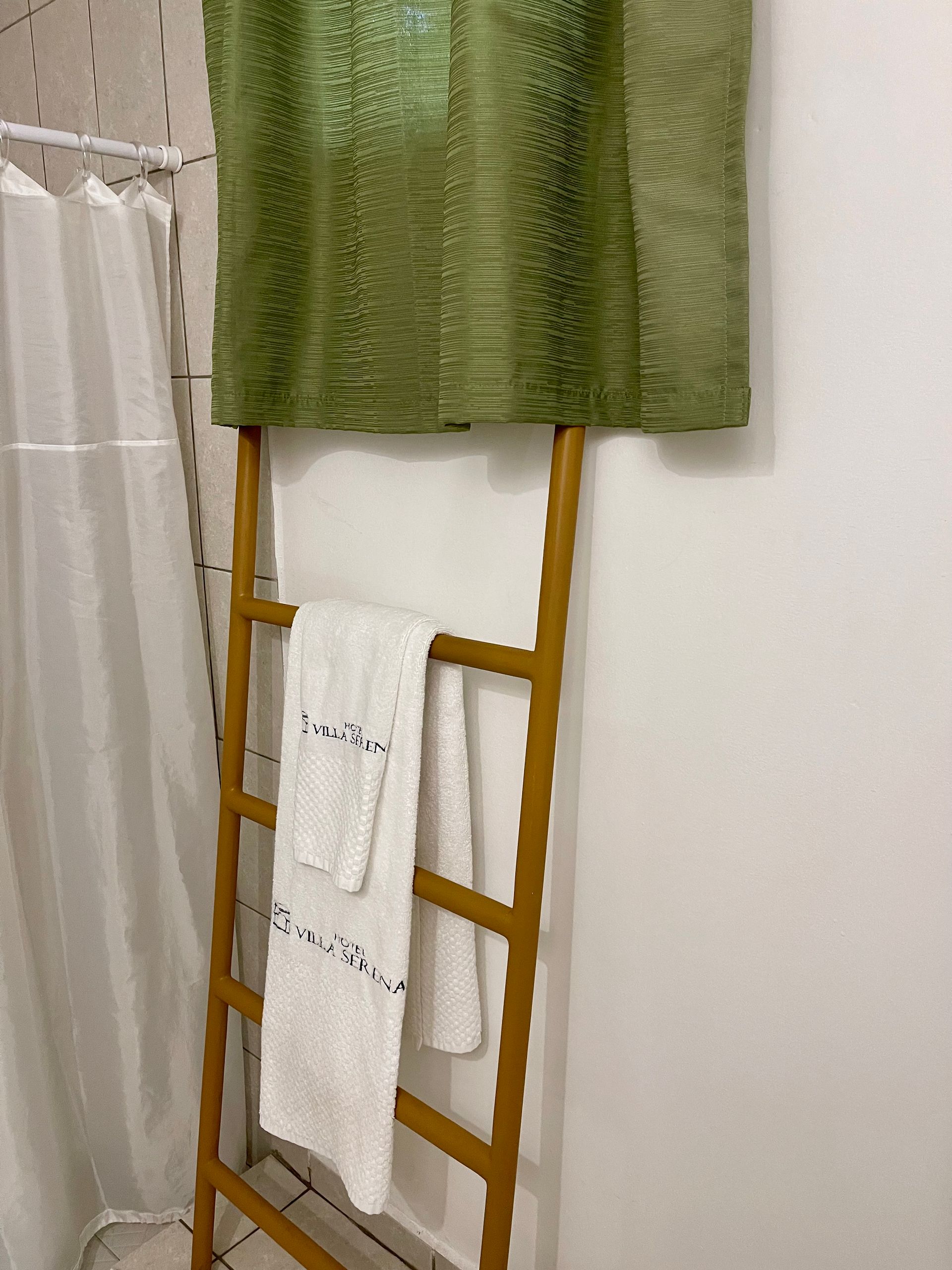 Two towels are hanging on a wooden ladder in a bathroom.