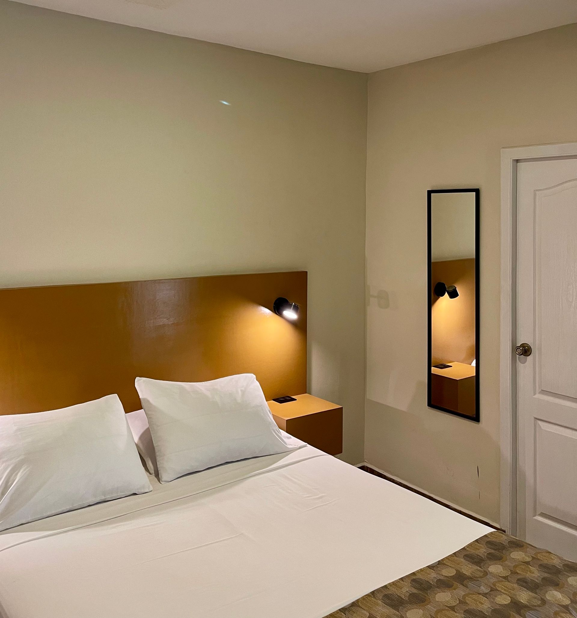 A hotel room with a bed and a mirror on the wall