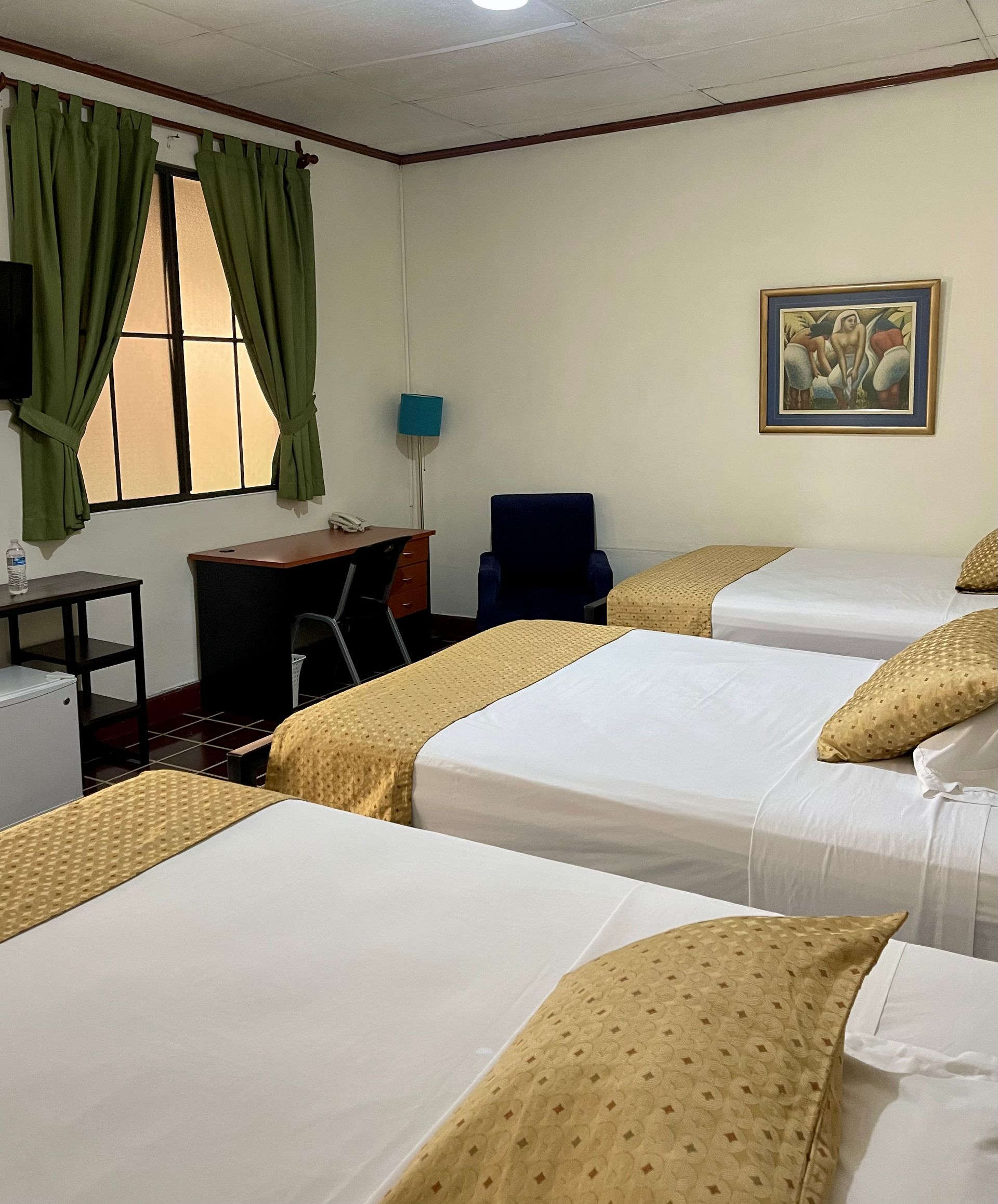 A hotel room with three beds , a desk and a chair.