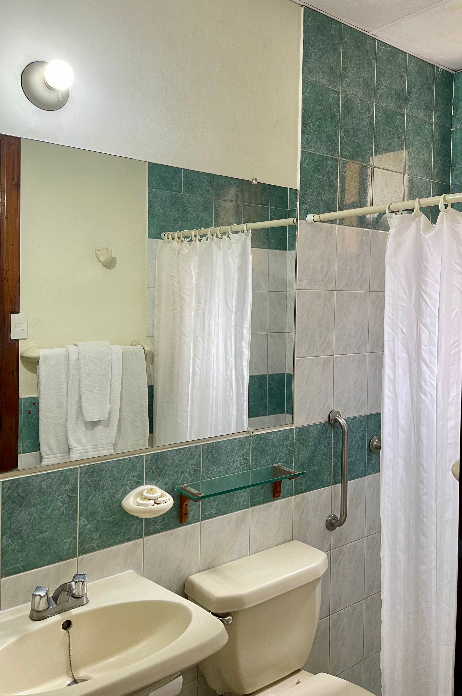 A bathroom with a toilet , sink , mirror and shower curtain.