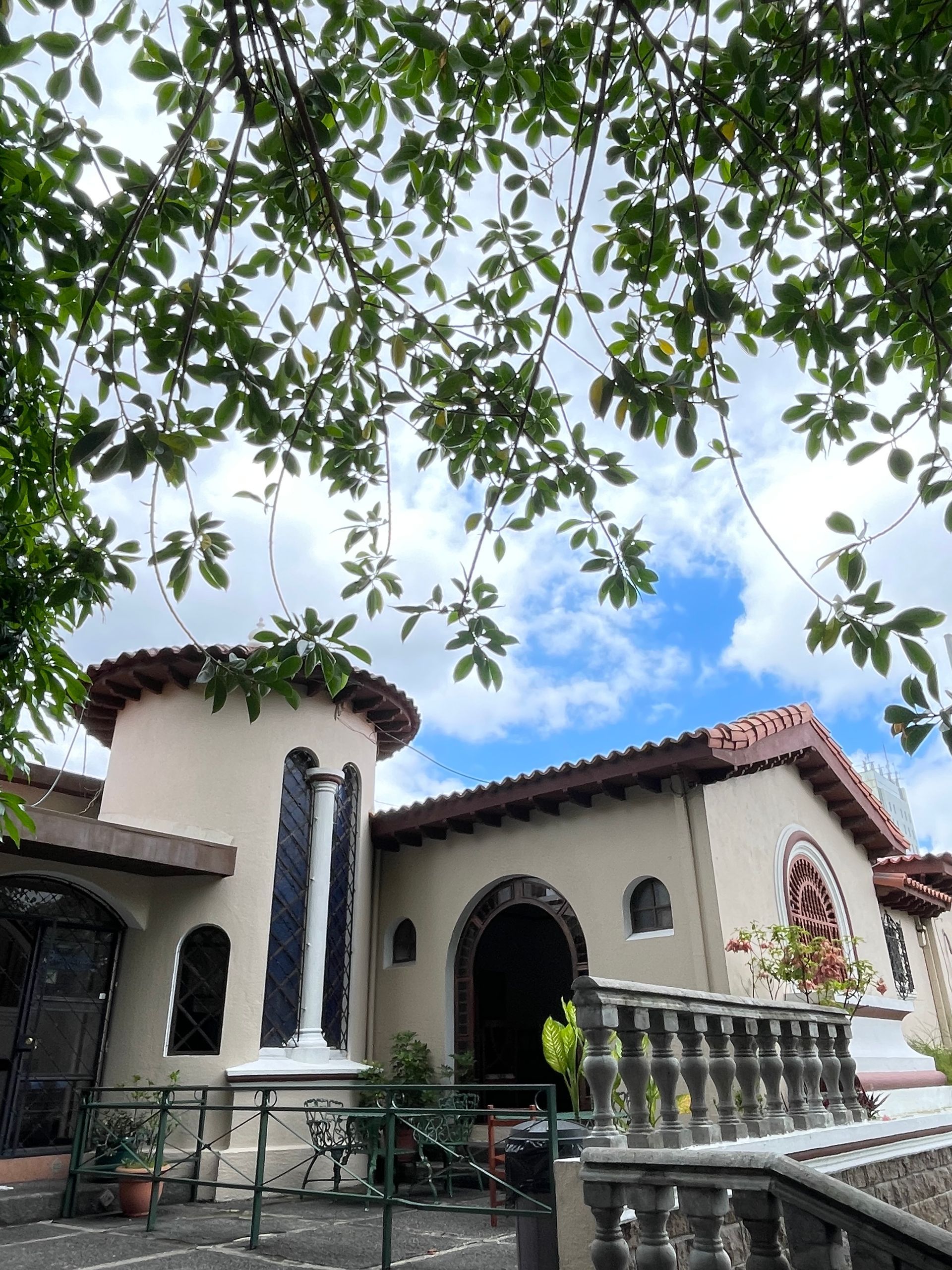 A large white house with a red tile roof is surrounded by trees.