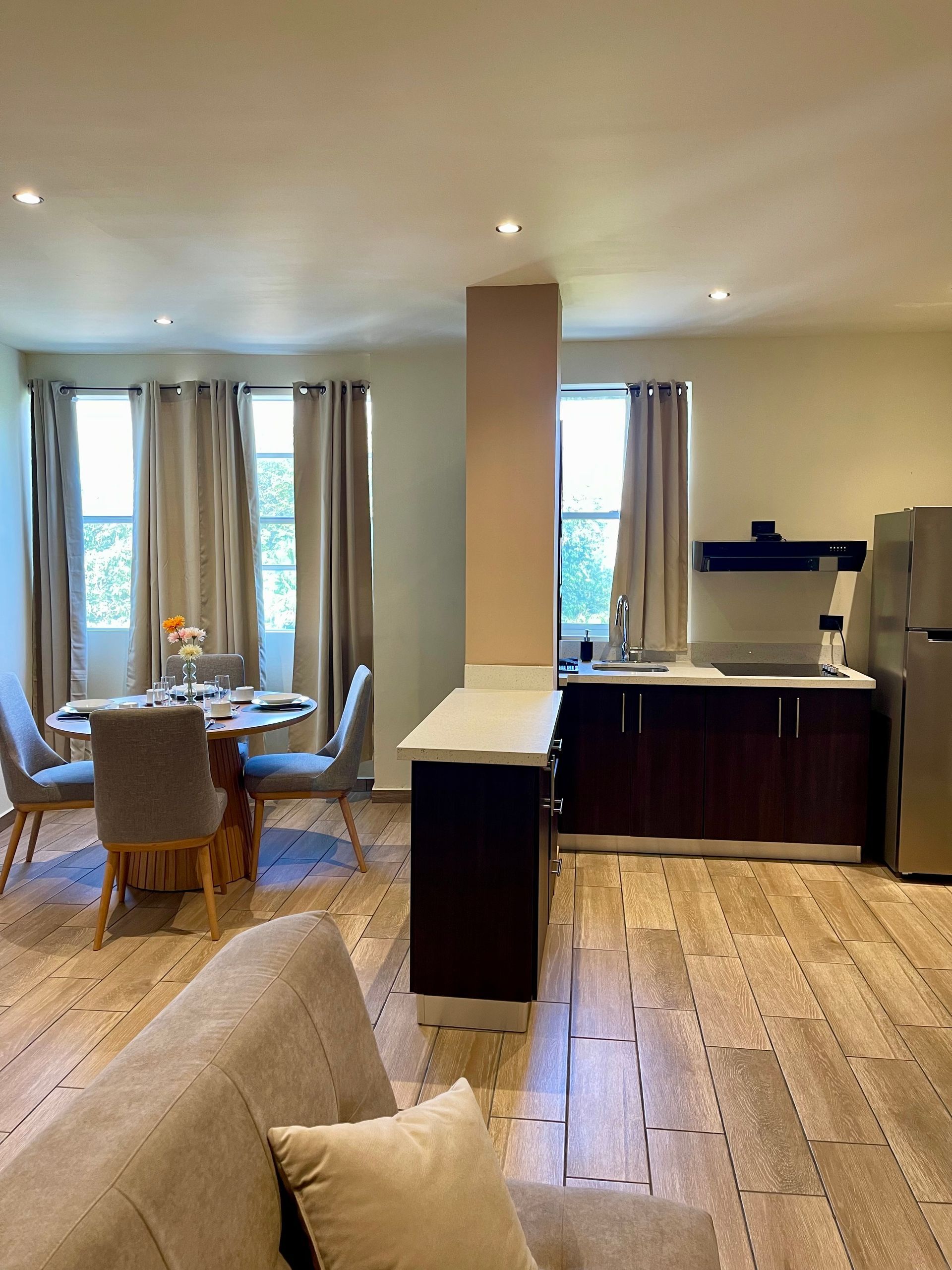 A living room with a couch , chairs , a table and a kitchen.