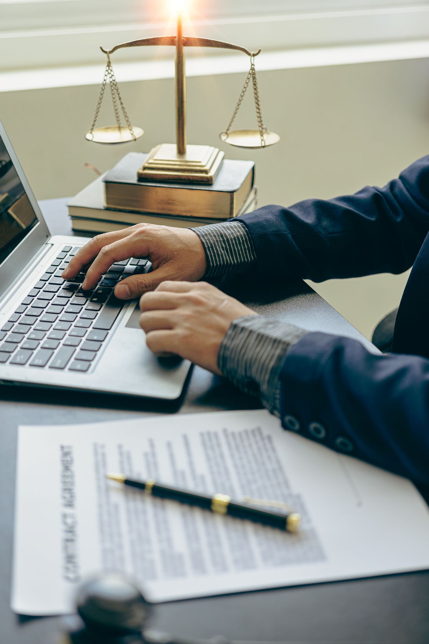 A man is typing on a laptop computer in front of a scale of justice.
