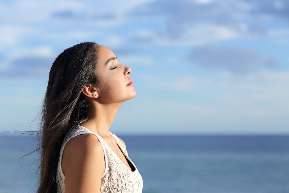 A Woman Is Standing On The Beach With Her Eyes Closed And Breathing Fresh Air — The Therapists Cairns In Cairns City, QLD