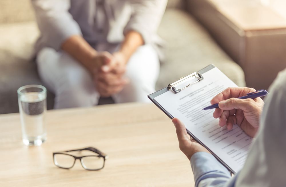 A Man Is Holding A Clipboard And A Pen While Talking To A Woman — The Therapists Cairns In Cairns City, QLD