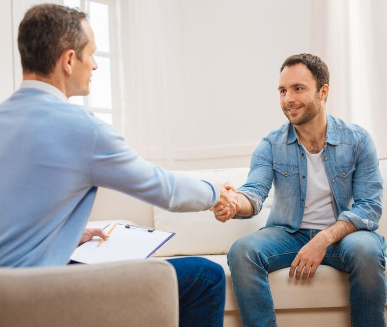 A Man Is Shaking Hands With Another Man While Sitting On A Couch — The Therapists Cairns In Cairns City, QLD