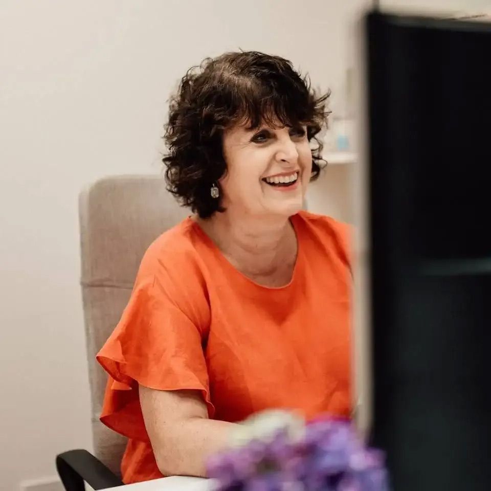 Accountant  In An Orange Shirt Is Smiling In Front Of A Computer — Dynamic Accounting Taxation Advisors in Terrigal, NSW