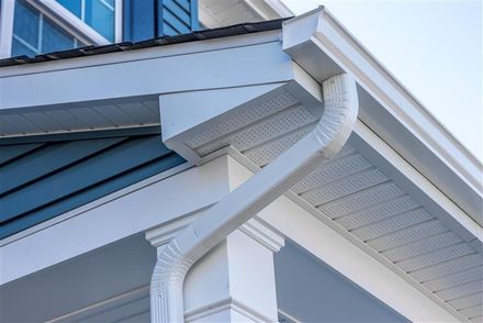 White gutter and downspout attached to the corner of a residential house with blue siding and a white column.