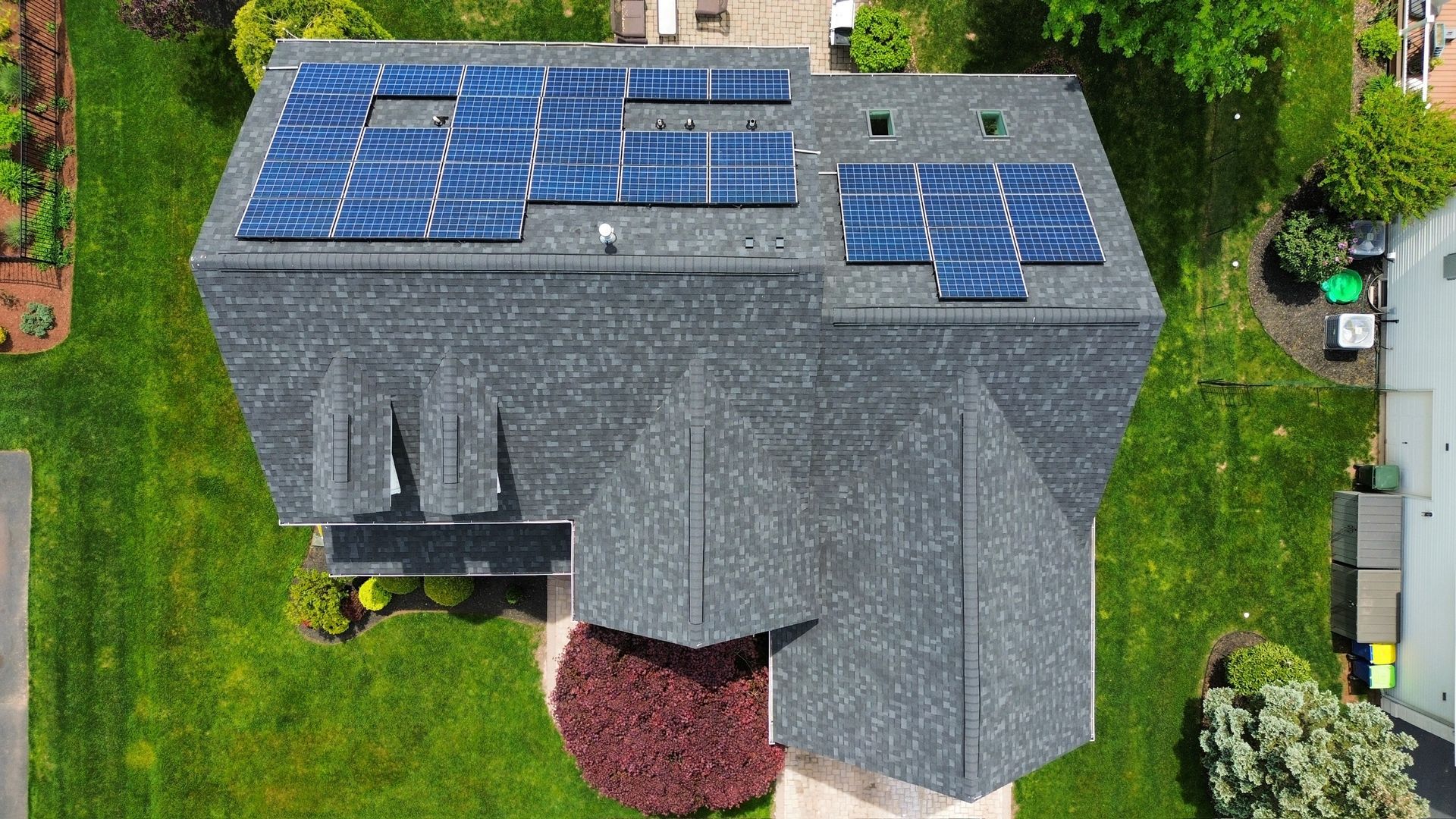 Aerial view of a gray shingled residential roof with two sets of solar panels installed on a sunny day.