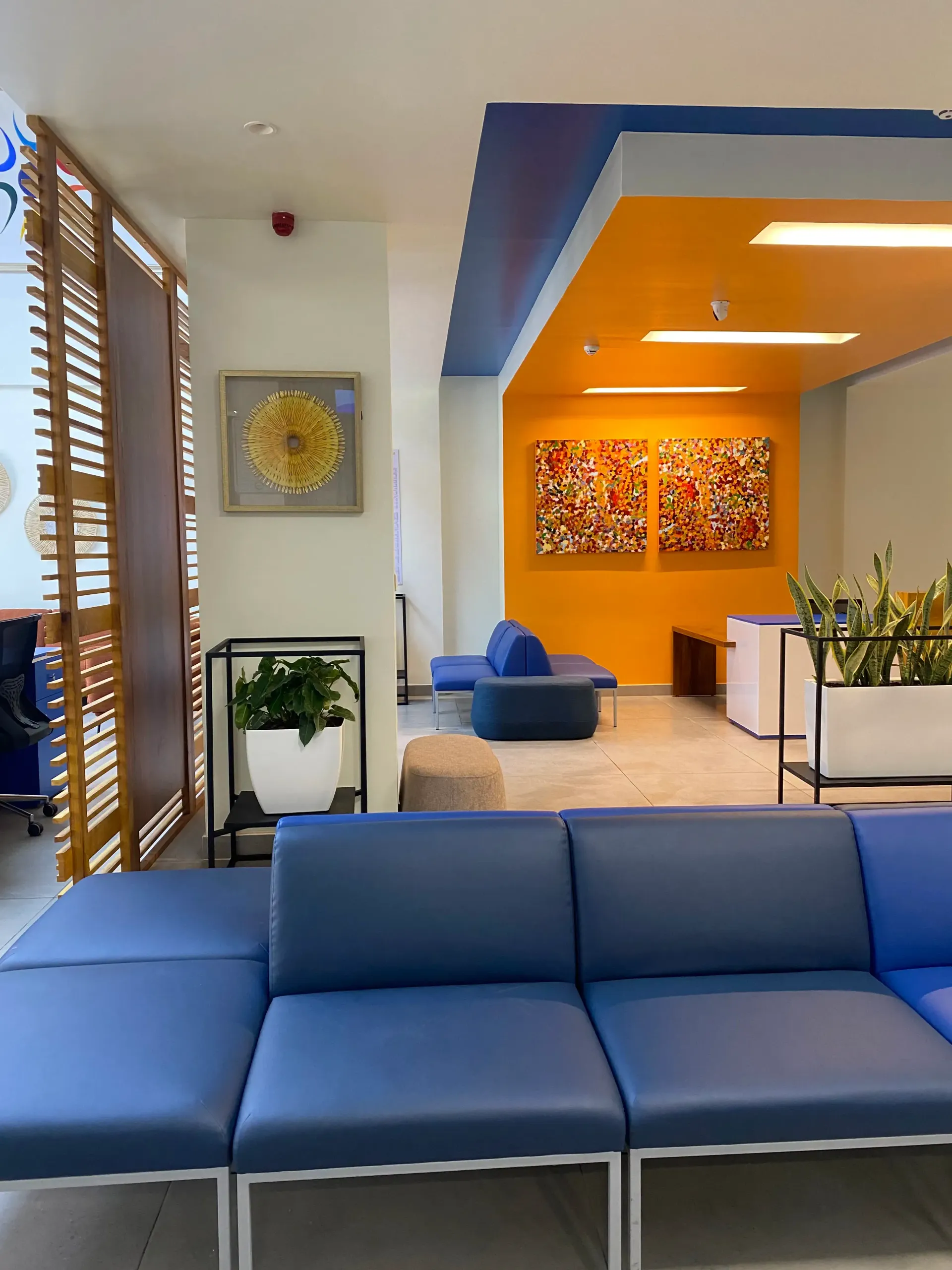 Une salle d'attente avec des canapés bleus et des tableaux au mur.