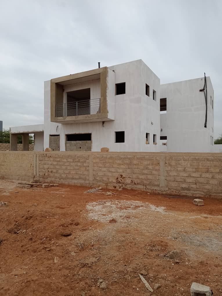 Une grande maison blanche est en construction au milieu d'un champ de terre.