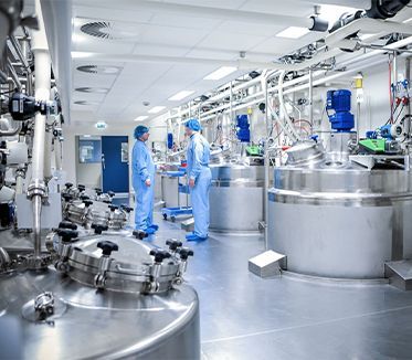 Deux hommes en blouse bleue se tiennent dans une usine entourée de cuves en acier inoxydable.