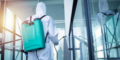 Un homme en combinaison de protection désinfecte un bâtiment avec un pulvérisateur.