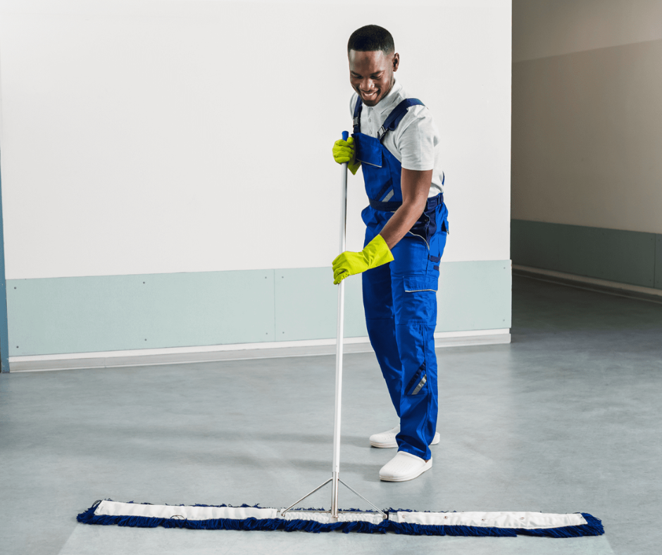 Un homme en salopette bleue nettoie le sol avec une serpillère.