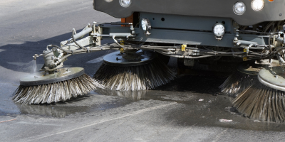 Un balayeur de rue nettoie la route avec des brosses.