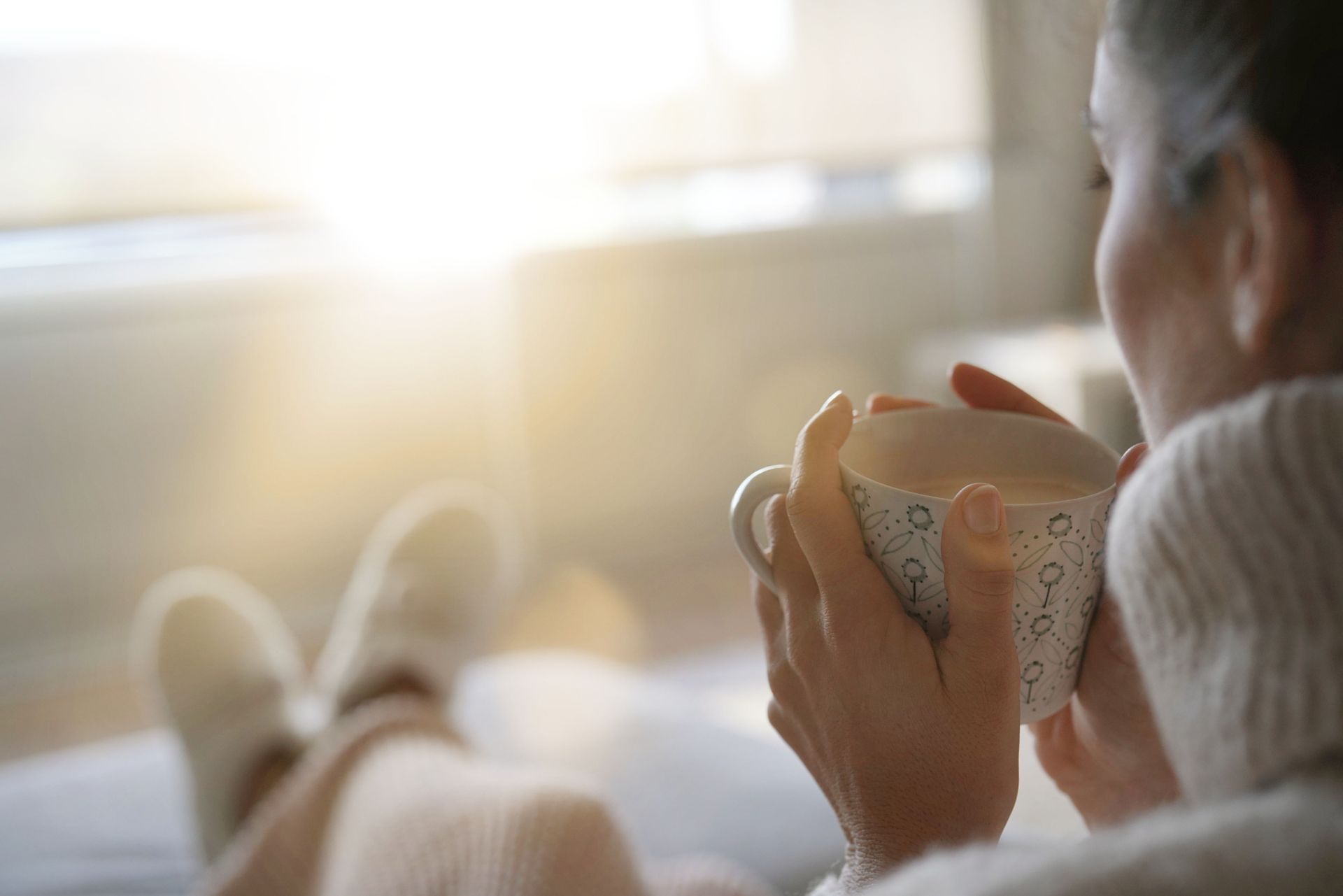 A woman is sitting on a couch drinking a cup of coffee.