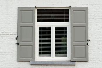 A white window with gray shutters on a white brick wall