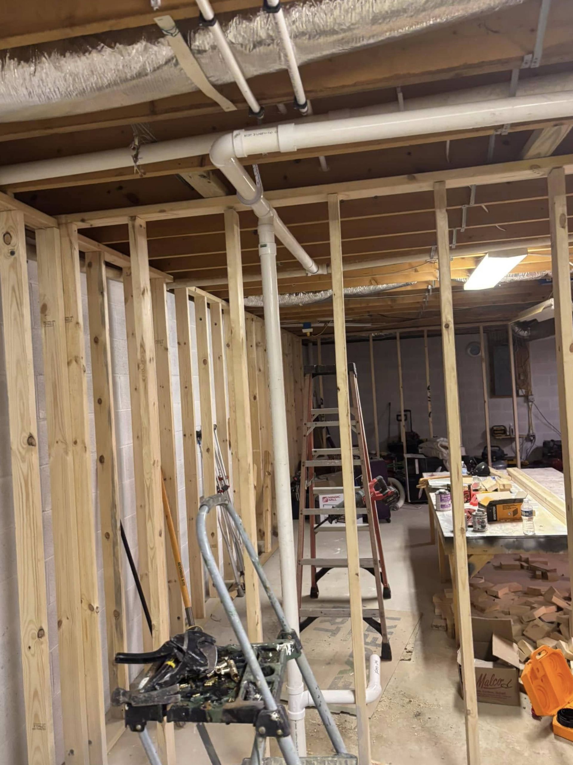 A basement under construction with pipes and a ladder.
