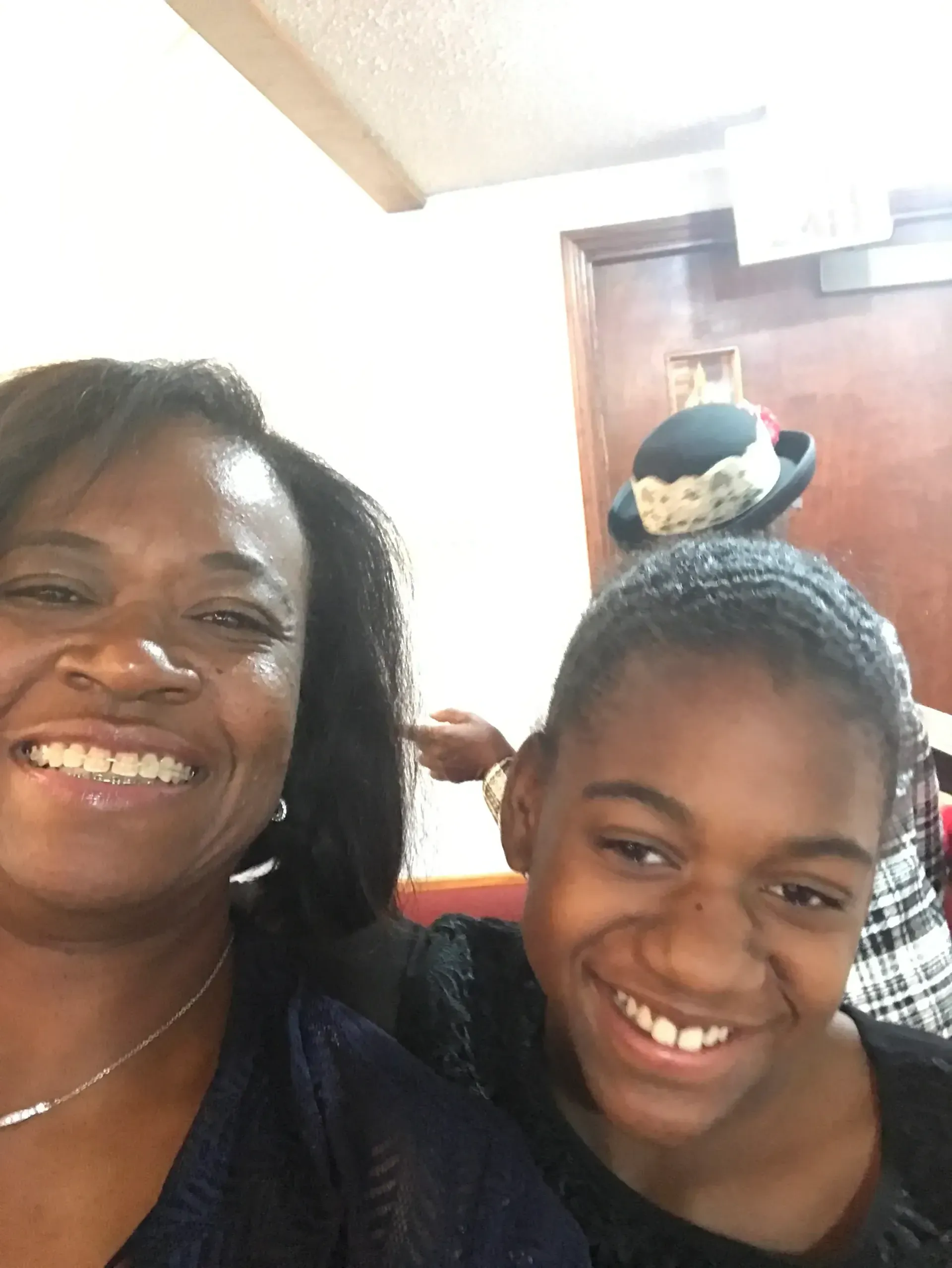 Woman and child smiling, indoors. Child wearing dark clothing, woman has dark hair and necklace.