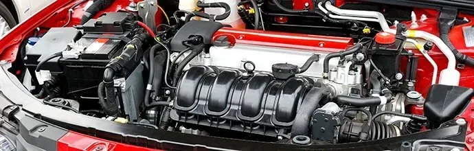 Close-up of a clean, bright red car engine bay featuring a prominent black intake manifold and various hoses and wires.