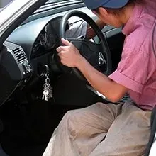 A person in a pink shirt and tan pants cleans the interior of a car steering wheel with a cloth.