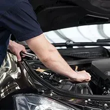 A mechanic works on a car engine under the open hood, using a ratchet tool to tighten a bolt.