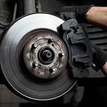 A mechanic wearing black gloves performs maintenance on a vehicle's disc brake system in a garage.