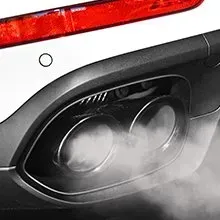 A close-up of a vehicle's dual exhaust tailpipes emitting a cloud of white smoke.