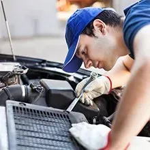 A mechanic wearing a blue cap and work gloves uses a wrench to repair the engine of a car.