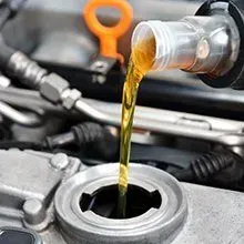 Clear, golden motor oil pours from a bottle into an open engine oil filler cap.