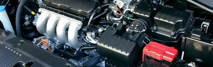 A view of a clean car engine bay featuring an intake manifold, air filter box, and a prominent red battery terminal cover.