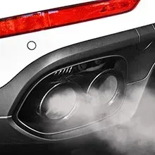 A close-up of a white vehicle's exhaust pipe emitting a cloud of white smoke beneath a red rear reflector.