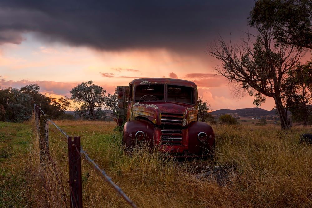 An Old Red Truck is Parked in a Field at Sunset — Southern Tablelands Windscreen Repairs In Marulan, NSW
