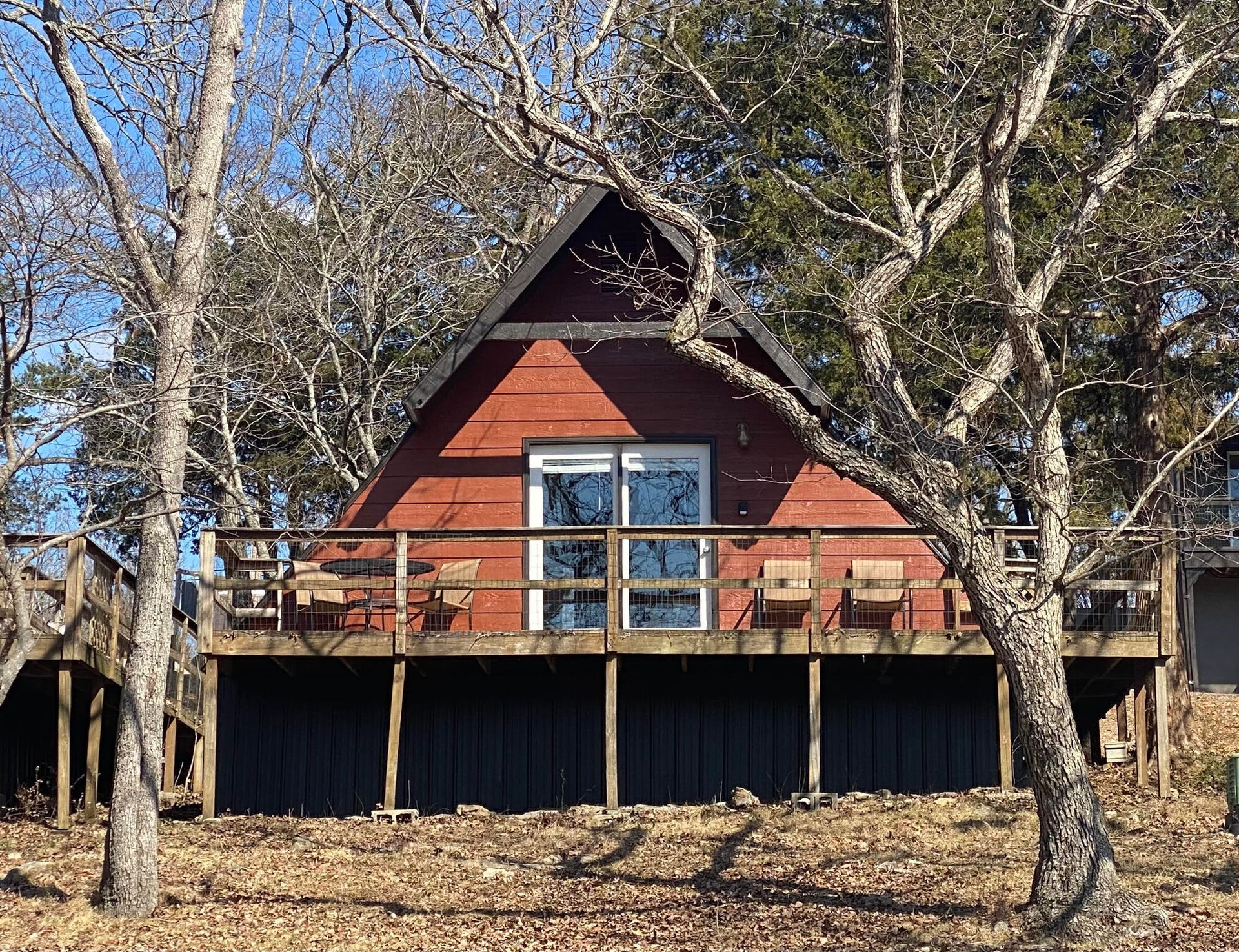 A-frame cabin with a red facade, black base, and deck. Trees frame the cabin.