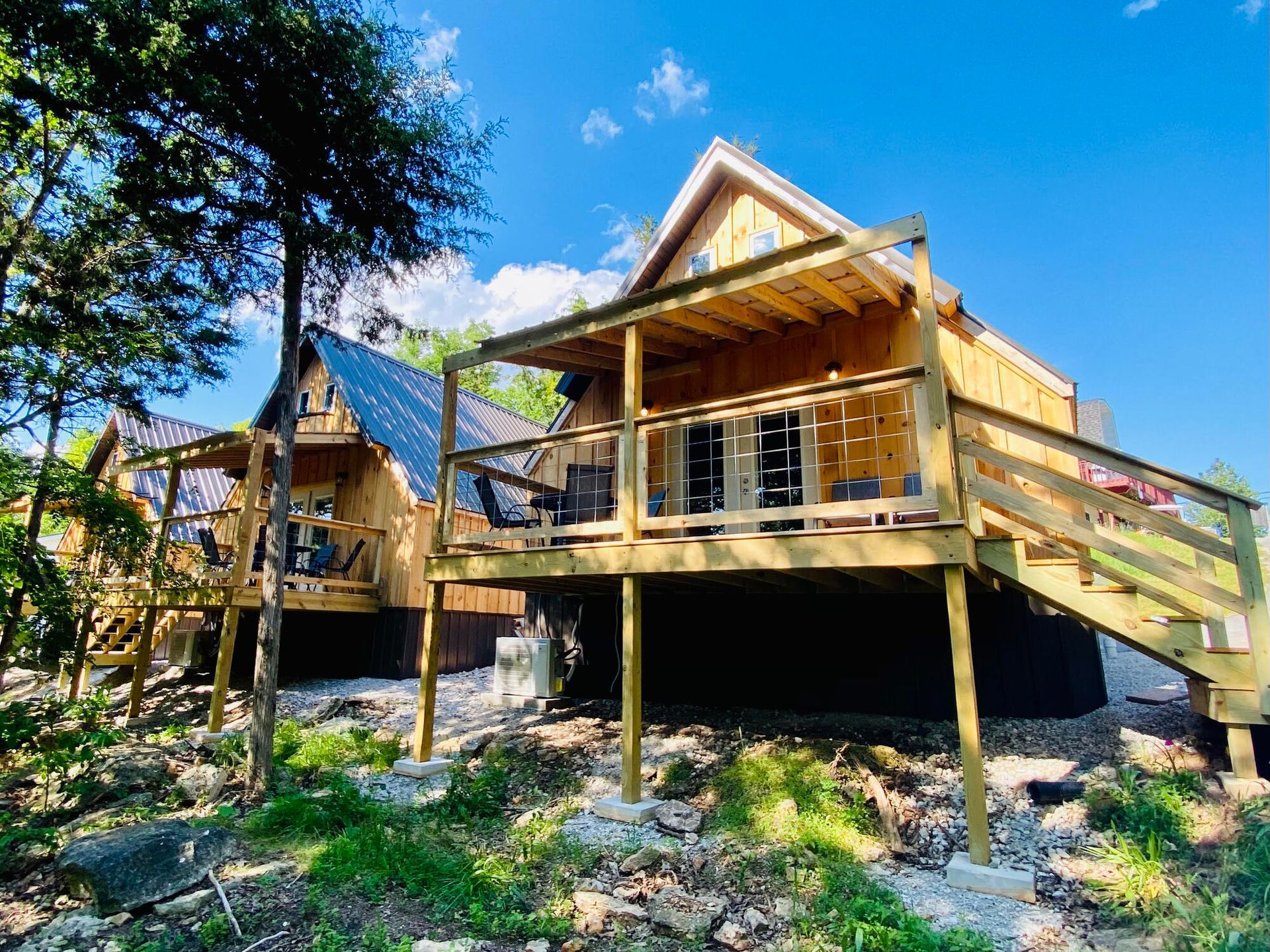 Wooden cabins with decks, nestled in a wooded area, under a bright, sunny sky.