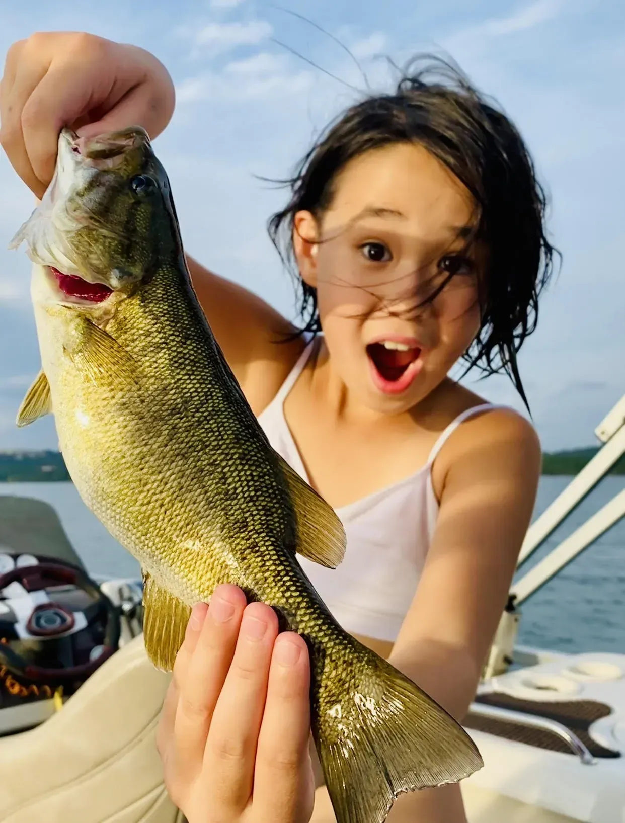 Girl holding a fish with an excited expression on a boat.