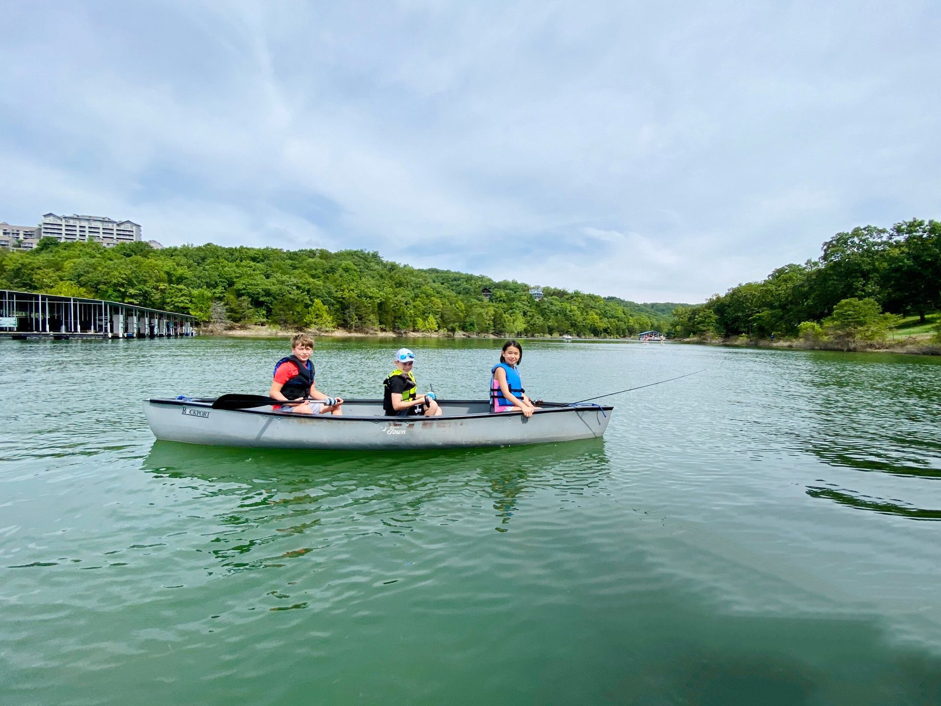 Three people paddling a canoe on a lake with green water and trees in the background.