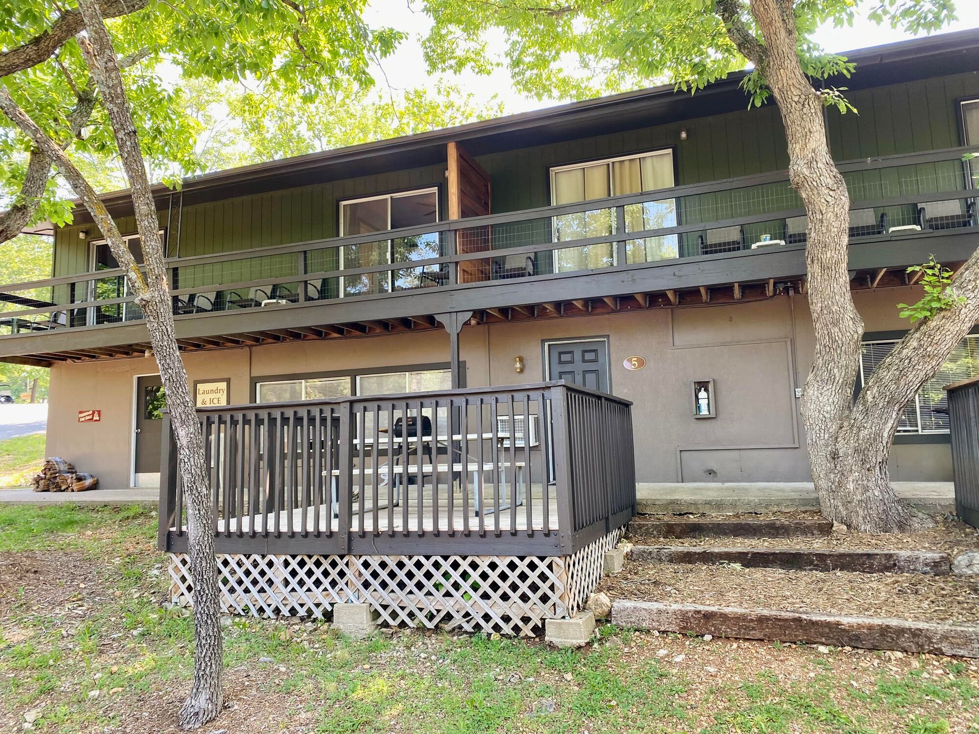 Two-story building with decks and brown siding. Trees frame the structure in a natural setting.