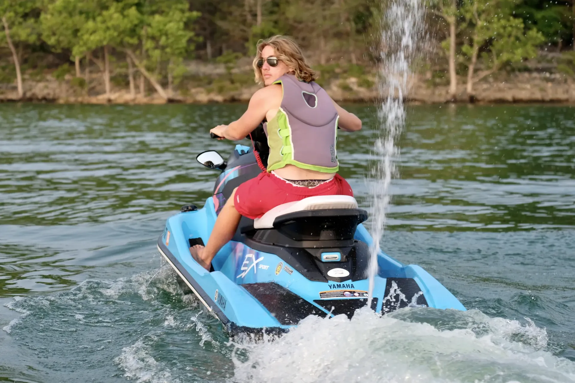 Woman on a blue jet ski, riding on water, wearing a life vest.