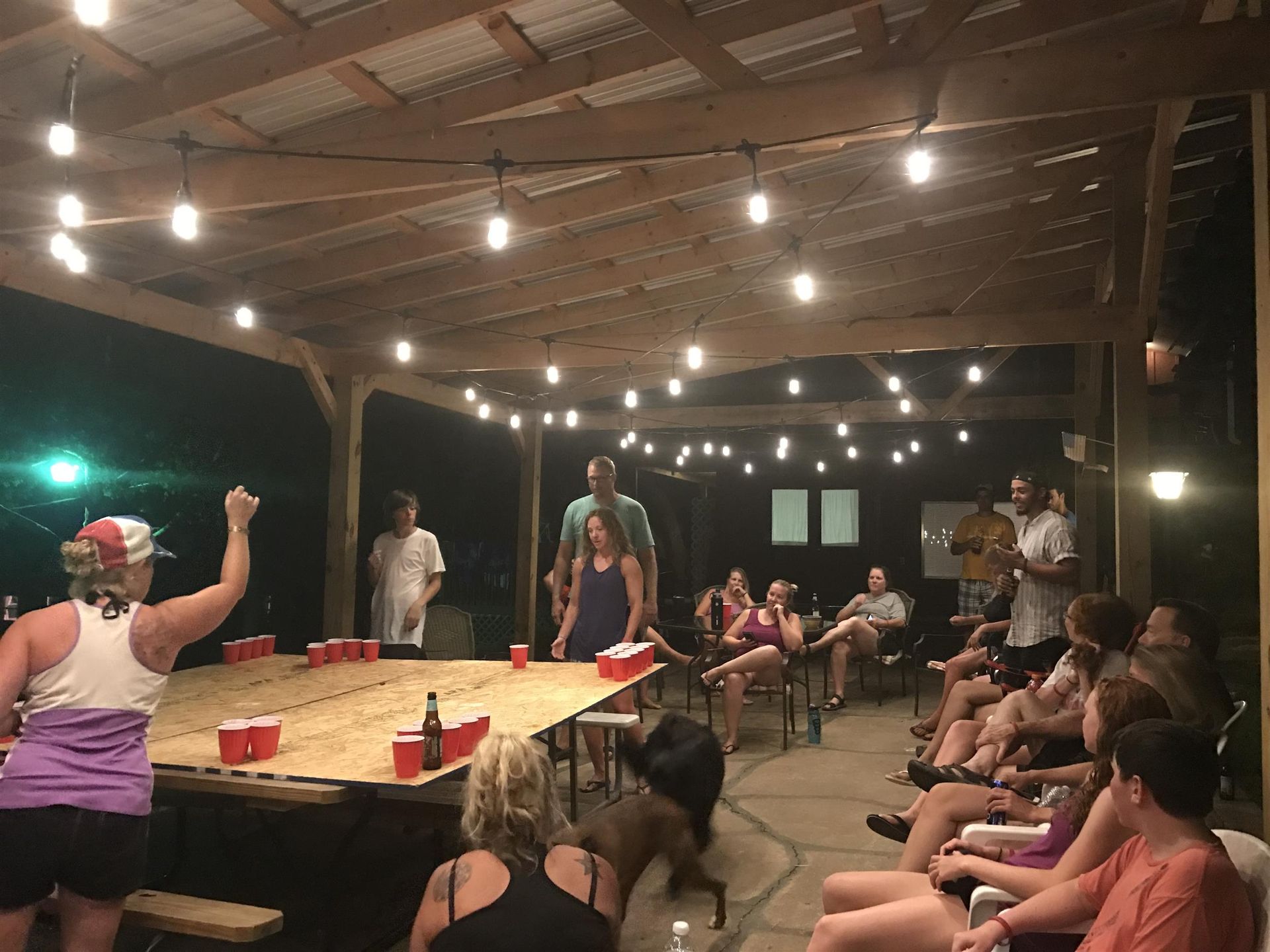 People playing beer pong under string lights on a covered patio at night.