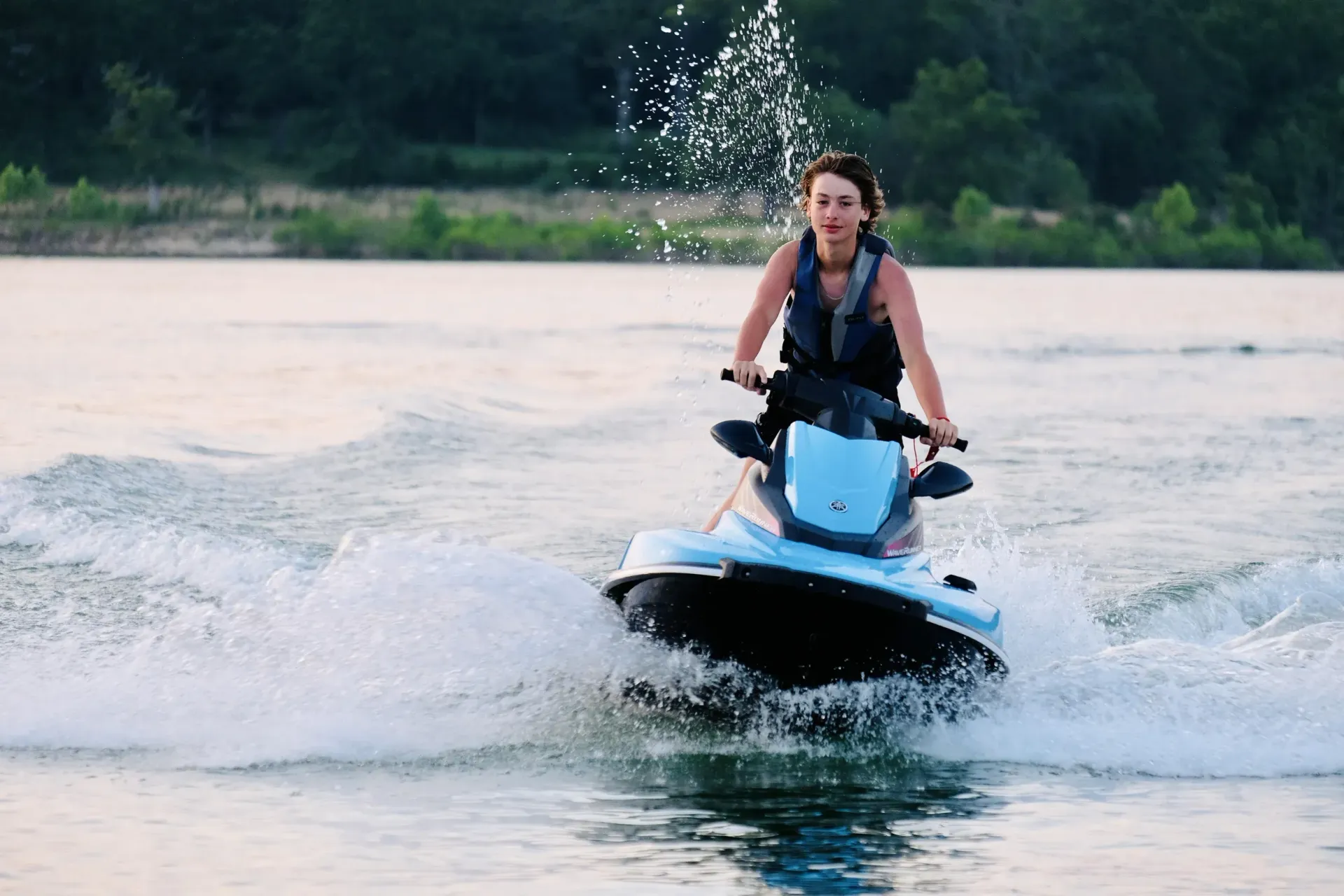 Woman and two children on a yellow jet ski on a body of water, all wearing life jackets.