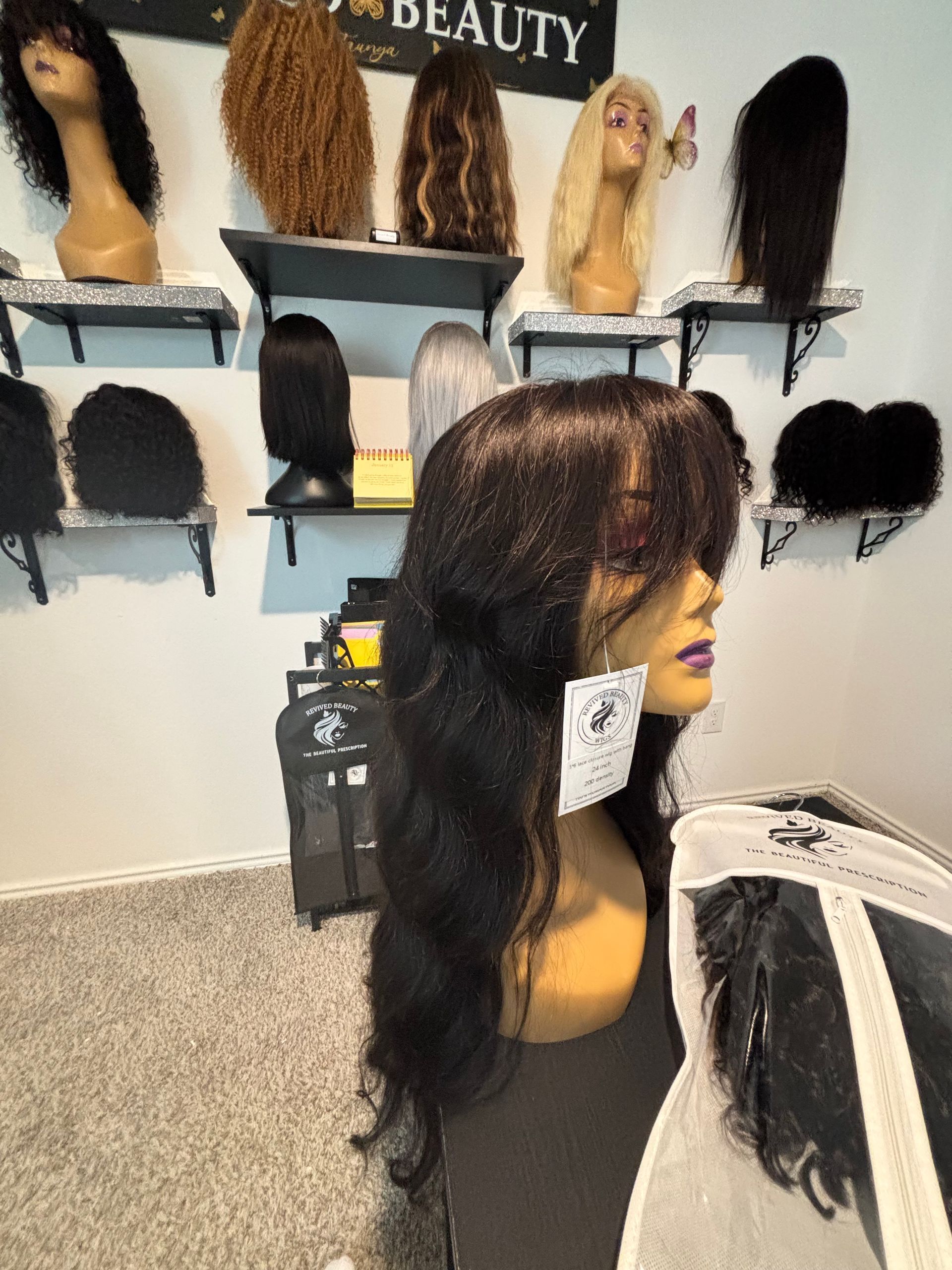 A mannequin with a long, wavy black wig with bangs, in a beauty store with various wigs on display.