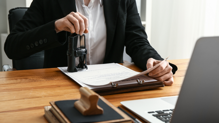Person in suit stamping a document on a desk next to a laptop.