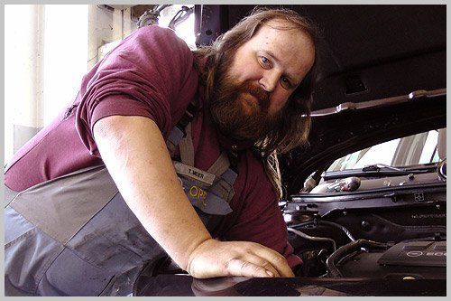 Ein Mann mit Bart schaut unter die Motorhaube eines Autos.