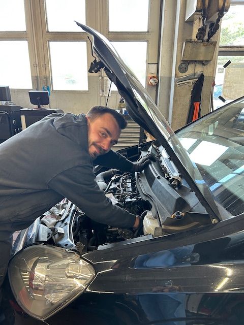 Ein Mann arbeitet am Motor eines Autos bei geöffneter Motorhaube