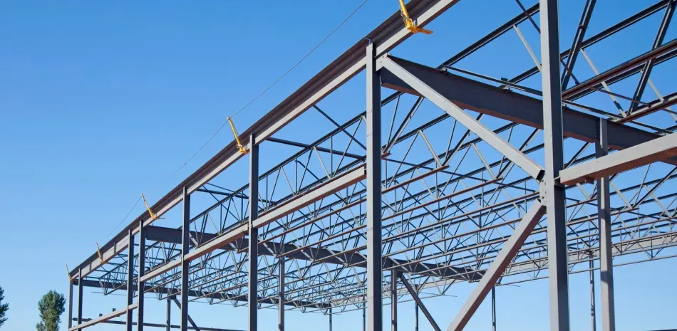 A large metal structure is under construction with a blue sky in the background.