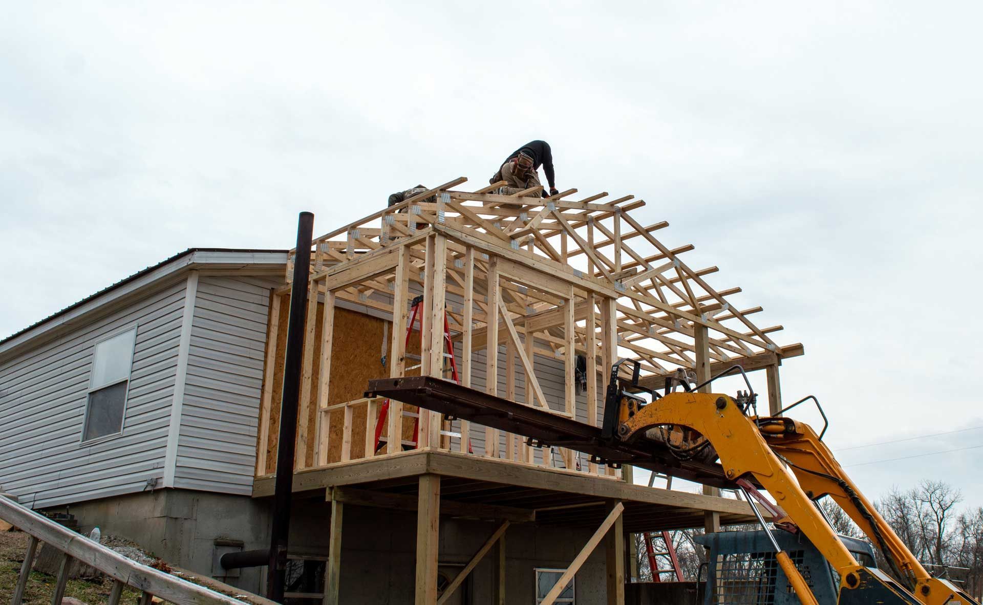 A house is being built and a forklift is lifting a piece of wood.
