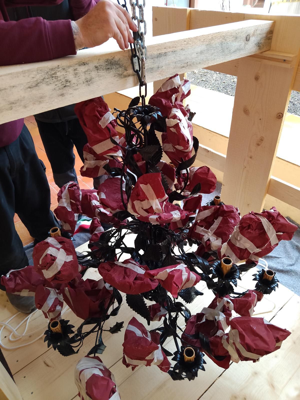 Lampadario ricoperto di carta rossa e bianca, appeso a una catena e tenuto in mano da una persona.